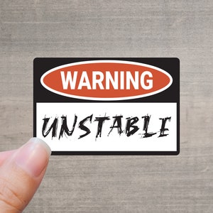 May include: A black and white warning sign with red text that reads "WARNING" and "UNSTABLE" in a bold, handwritten font.