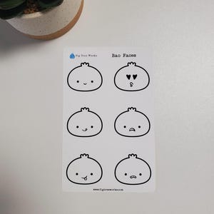 May include: A sheet of black and white stickers featuring six different bao bun faces with various expressions. The text "Bao Faces" and "Fig Tree Works" are printed at the top of the sheet.
