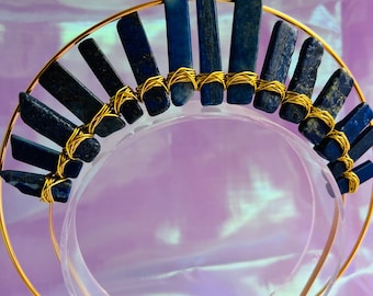 May include: A gold headband with a row of blue lapis lazuli stones wrapped in gold wire. The stones are arranged in a semi-circle shape.