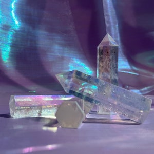 May include: Four clear quartz crystal points with iridescent rainbow colors. The crystals are arranged in a cluster on a purple iridescent fabric background.
