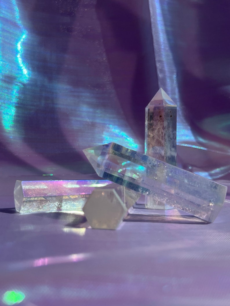 May include: Four clear quartz crystal points with iridescent rainbow colors. The crystals are arranged in a cluster on a purple iridescent fabric background.