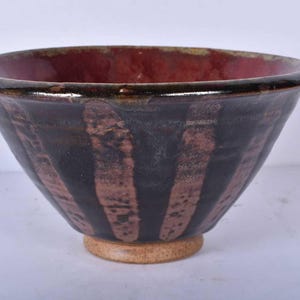 May include: A handcrafted ceramic bowl. It has a dark red interior and a black exterior with vertical brown stripes. The bowl has a rounded base and a wide rim, ideal for serving food.