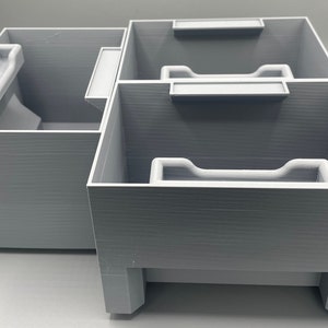 Peut inclure: Un organisateur en plastique gris avec trois compartiments. Chaque compartiment est doté d'un séparateur en plastique blanc. L'organisateur a une surface texturée.