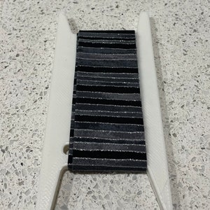 Könnte beinhalten: Ein weißer Kunststoff-Spulenhalter mit einem schwarz-silbernen gestreiften Band.