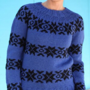 May include: A blue knitted jumper featuring black geometric designs. The jumper has a round neck and long sleeves. The black patterns are arranged in horizontal bands across the chest, sleeves, and upper torso. The jumper is made of a soft, warm material.