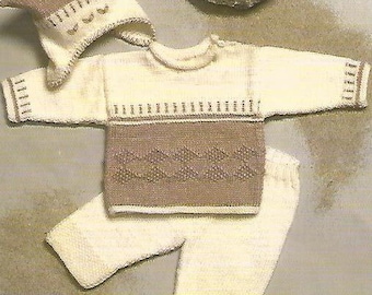 Puede incluir: Un conjunto de bebé tejido en crema y marrón, que incluye un gorro, un suéter y pantalones. El suéter presenta una banda marrón en el pecho y un diseño estampado en la parte inferior. El gorro tiene un ribete decorativo.