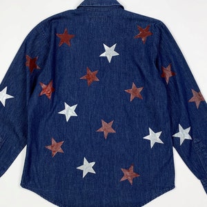 K&ouml;nnte beinhalten: Ein dunkelblaues Jeanshemd mit langen &Auml;rmeln und Knopfleiste. Das Hemd ist mit wei&szlig;en und kastanienbraunen Sternen verziert.