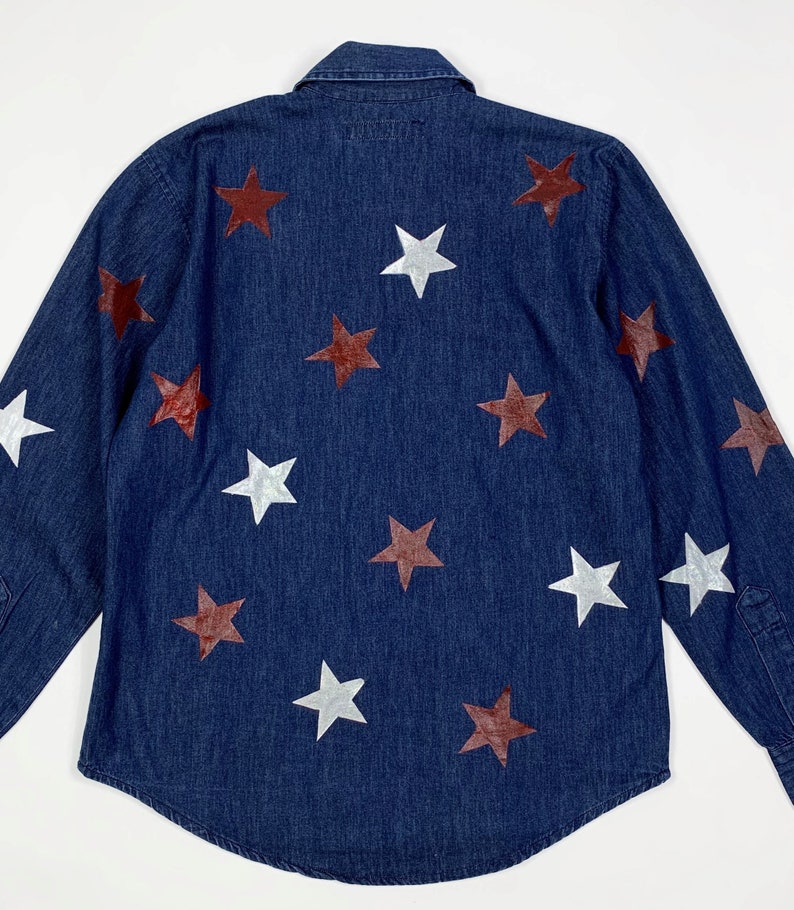 K&ouml;nnte beinhalten: Ein dunkelblaues Jeanshemd mit langen &Auml;rmeln und Knopfleiste. Das Hemd ist mit wei&szlig;en und kastanienbraunen Sternen verziert.