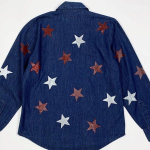 K&ouml;nnte beinhalten: Ein dunkelblaues Jeanshemd mit wei&szlig;en und kastanienbraunen Sternen, die auf der Vorderseite aufgedruckt sind.