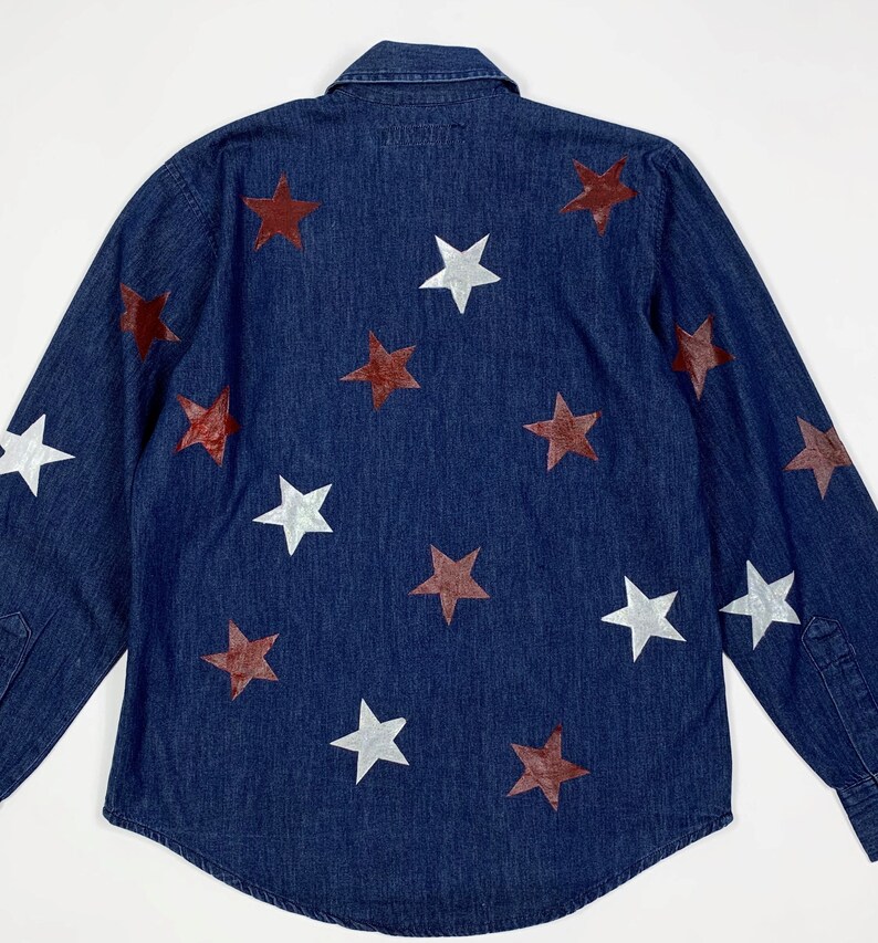 K&ouml;nnte beinhalten: Ein dunkelblaues Jeanshemd mit wei&szlig;en und kastanienbraunen Sternen, die auf der Vorderseite aufgedruckt sind.