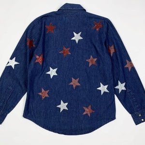 K&ouml;nnte beinhalten: Ein dunkelblaues Jeanshemd mit langen &Auml;rmeln und Knopfleiste. Das Hemd ist mit wei&szlig;en und kastanienbraunen Sternen verziert.