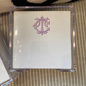 May include: A clear acrylic box with a white card inside. The card has a purple monogram with the letters "T.L." in a decorative font.