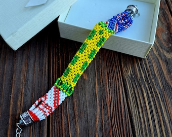 Può includere: Un braccialetto di perline colorato con perline gialle, verdi, rosse, bianche e blu. Il braccialetto è presentato in una confezione regalo bianca con un fiocco argentato. Il braccialetto è fatto di piccole perline e ha una chiusura argentata.