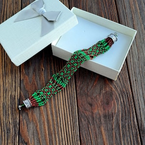 May include: A green and brown beaded bracelet with silver end caps, displayed in a white gift box with a white satin bow.
