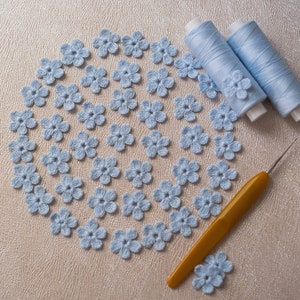 Peut inclure: Gros plan sur un cercle de fleurs crochetées bleu clair, avec deux bobines de fil et un crochet en arrière-plan.