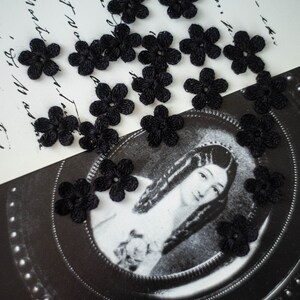 Peut inclure: Une collection de petites fleurs crochetées noires éparpillées sur une surface blanche avec une photo en noir et blanc d'une femme en arrière-plan.