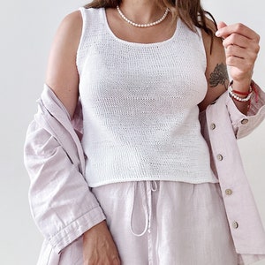 Peut inclure: Un débardeur blanc en tricot avec un col rond et un ensemble chemise et short en lin rose clair.