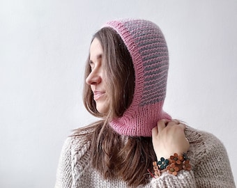 Puede incluir: Una balaclava de punto a rayas rosa y gris con un borde doblado. La balaclava la lleva puesta una persona con el pelo largo y castaño. La persona lleva un jersey de punto beige y una pulsera de cuero marrón con detalles de flores verdes.
