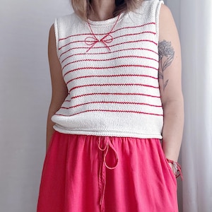 May include: A sleeveless white and red striped knit top and a bright pink skirt. A red bow necklace is worn. The skirt has a drawstring waist. The outfit is casual and summery.