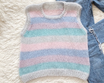 Puede incluir: Un chaleco de punto sin mangas con rayas horizontales en tonos pastel de rosa, azul, verde menta y gris. La prenda tiene un cuello redondo y una textura esponjosa. Junto al chaleco se encuentran unos vaqueros azules y varios accesorios.