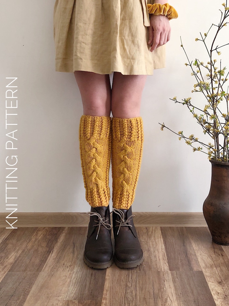 May include: A pair of yellow knitted leg warmers with a cable knit pattern. The leg warmers are worn over brown boots.