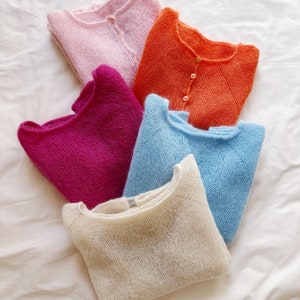 May include: Five knitted sweaters in different colors: pink, orange, magenta, light blue, and cream. The sweaters are folded and stacked on top of each other.