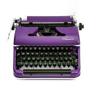 May include: A vintage purple typewriter with a black keyboard and the word "Olympia" printed on the front.