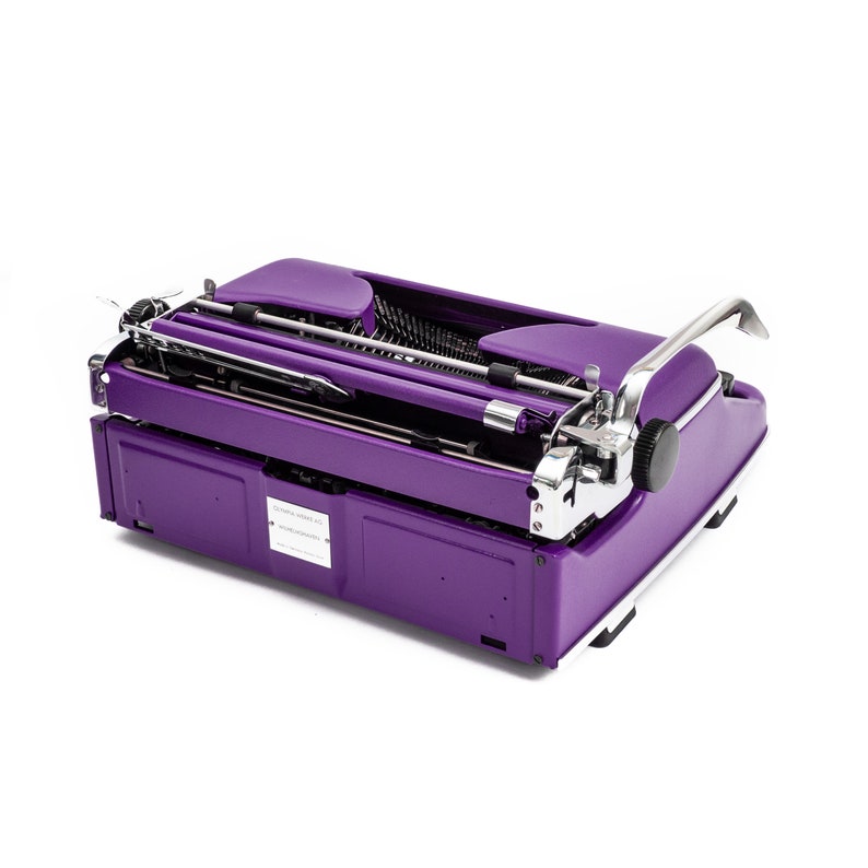 May include: A purple vintage typewriter with a chrome carriage return lever and a silver nameplate that reads "Olivetti Lettera 32".