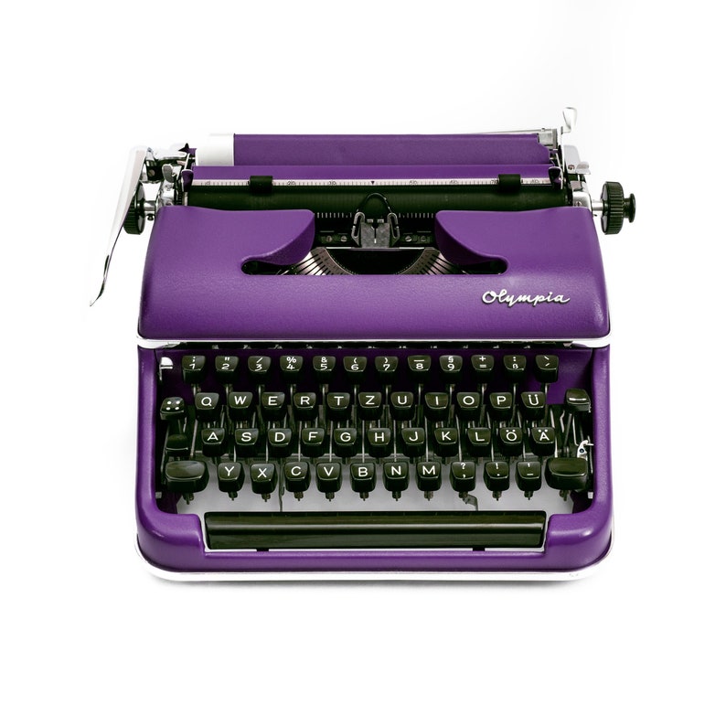 May include: A vintage purple typewriter with a black keyboard and the word "Olympia" printed on the front.