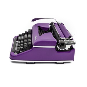 May include: A purple vintage typewriter with a black keyboard and chrome accents. The typewriter is in a side view, showing the carriage return lever and the paper roller.