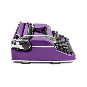 May include: A purple vintage typewriter with a black keyboard and chrome accents. The typewriter is in a side view, showing the carriage return lever and the paper roller.