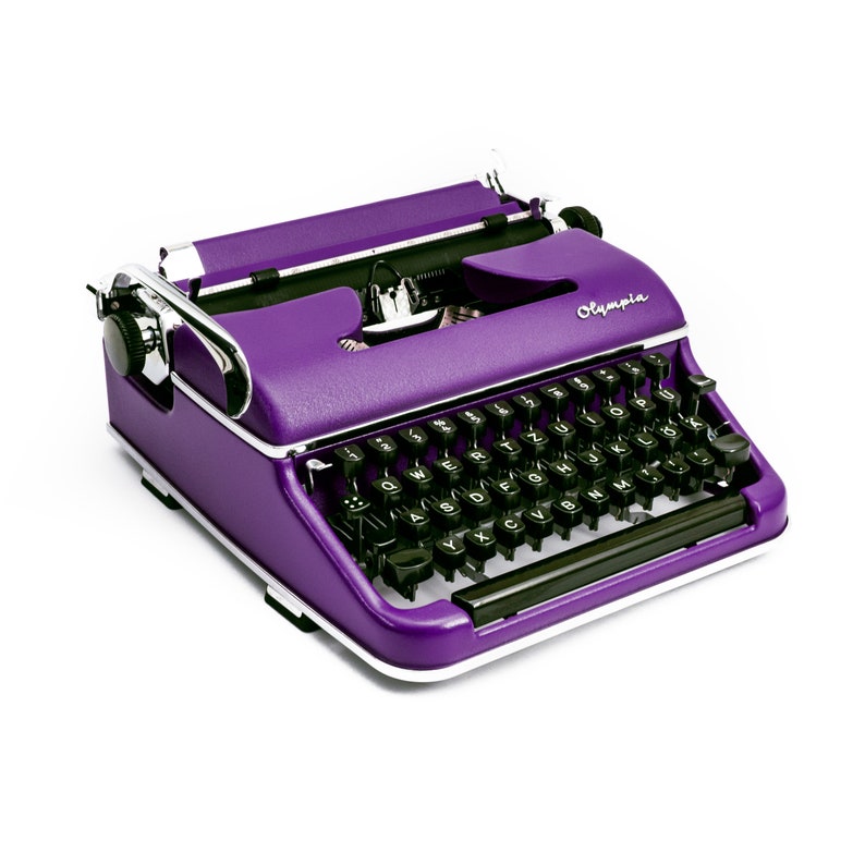 May include: A vintage purple typewriter with black keys and a silver carriage return lever. The typewriter has the word "Olympia" printed on the side.