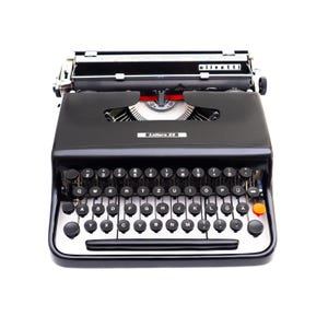 May include: A black Olivetti Lettera 22 typewriter with a silver trim. The typewriter features a full keyboard with black keys and white lettering. The carriage return lever is orange. The word "olivetti" is visible on the top.