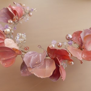 Puede incluir: Una delicada pieza de pelo floral rosa y blanca con detalles de perlas y cristales. La pieza está hecha de flores de tela y alambre.