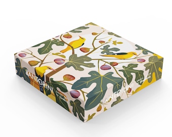 Op de afbeelding: Een vierkante doos met een lichtroze achtergrond en een patroon van groene bladeren, gele vogels en paarse vijgen. De doos heeft de tekst "SANTORINI SMALL BATCH by Claudia Gray" aan de zijkant.
