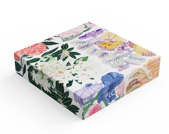 Op de afbeelding: Een witte doos met een bloemenontwerp met verschillende bloemen in tinten roze, paars, blauw, geel en oranje. Op de voorkant van de doos staat het woord "FLORAL".