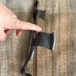 Könnte beinhalten: Ein Paar antike Metall-Brenneisen mit dunklem, verwittertem Aussehen. Die Eisen haben eine markante Form mit einem gebogenen Griff und einem flachen, rechteckigen Brennkopf. Das Design deutet auf eine rustikale oder Vintage-Ästhetik hin.