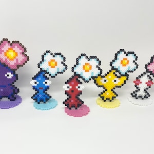 May include: A set of six colourful pixel art figures with flowers on their heads. The figures are made of small plastic beads and are arranged in a row on a white background.