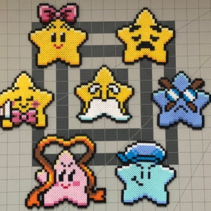 May include: Seven colorful star-shaped pixel art figures with different expressions and accessories. The figures are made of small plastic beads and are arranged in a grid pattern on a gray surface.