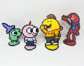 Può includere: Quattro figure colorate in pixel art, ciascuna in piedi su una base. Le figure sono un mago verde, una creatura rosa con una camicia bianca e jeans blu, una creatura gialla con un cappello marrone e una camicia arancione, e una creatura rossa con una cravatta blu.