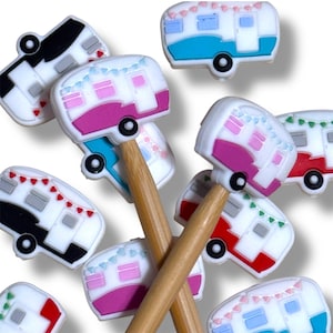 May include: A collection of colorful camper-shaped pencil toppers. Each topper features a white base with accents of pink, blue, red, and black. The campers have small black wheels and are decorated with tiny bunting flags. The pencils are made of wood.