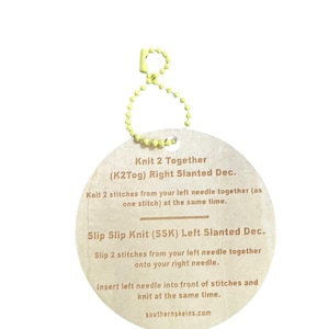 May include: A round, light brown tag with knitting instructions, attached to a yellow beaded chain. The tag features text detailing "Knit 2 Together" and "Slip Slip Knit" techniques, with the website southernskeins.com at the bottom.