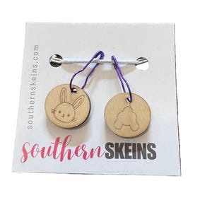 May include: Two wooden stitch markers with purple clasps. One marker features a bunny face, the other a bunny's rear. The markers are attached to a white card with the text "southernskeins.com" and "southern SKEINS" in pink.