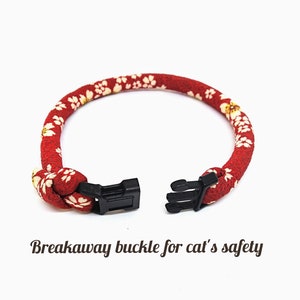 May include: Red and white floral patterned cat collar with a black breakaway buckle. "Breakaway buckle for cat's safety" is written below the collar.