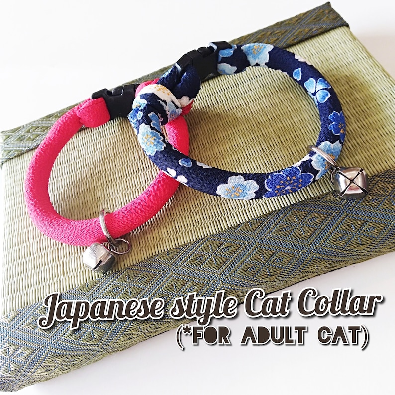 May include: Two Japanese-style cat collars with bells. One collar is pink and the other is blue with a floral pattern. The collars are on a woven mat with the text "Japanese style Cat Collar (*FOR ADULT CAT)".