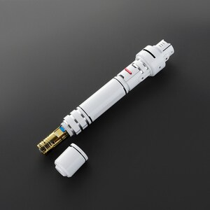 May include: A white and silver handheld device with a red button and a removable end cap. The device is open, revealing a gold-colored interior.