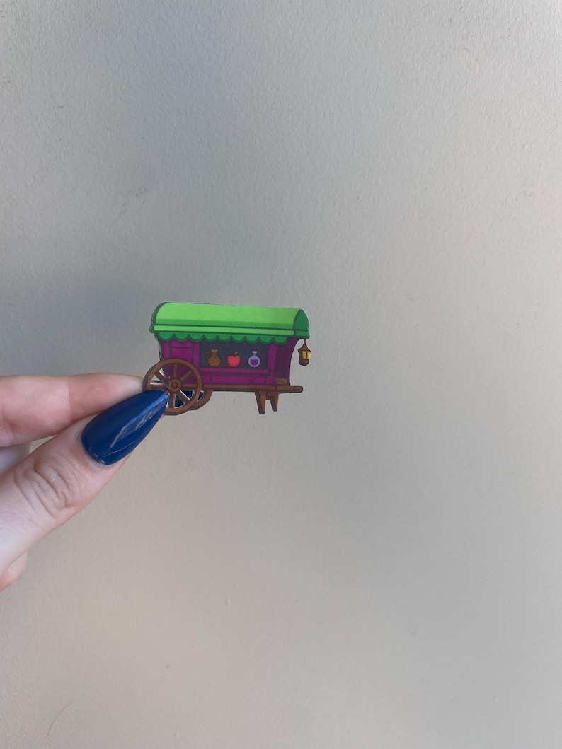 Puede incluir: Un vag&oacute;n en miniatura colorido con techo verde y cuerpo morado. El vag&oacute;n presenta una rueda de madera, peque&ntilde;os objetos decorativos y una linterna colgante. El dise&ntilde;o es caprichoso y de dibujos animados, con un enfoque en colores brillantes y detalles l&uacute;dicos.