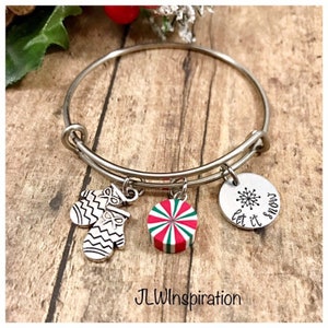 May include: Silver bangle bracelet with charms, including a peppermint candy, a pair of mittens, and a round charm with a snowflake and the text "Let it snow".
