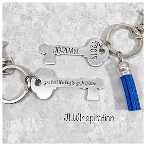 Op de afbeelding: Twee zilveren sleutelhangers met een blauwe kwast. De bovenste sleutelhanger heeft de tekst "JORDAN 2018" erop. De onderste sleutelhanger heeft de tekst "you hold the key to your future".