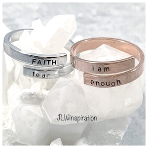 May include: Two silver and rose gold rings with inspirational messages. The silver ring says "FAITH over fear" and the rose gold ring says "i am enough".